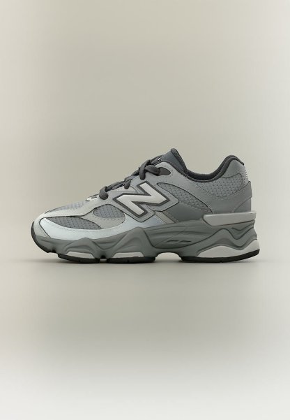 Zapatilla New Balance gris y negra con paneles de malla y cuero, suela gruesa y diseño con cordones.