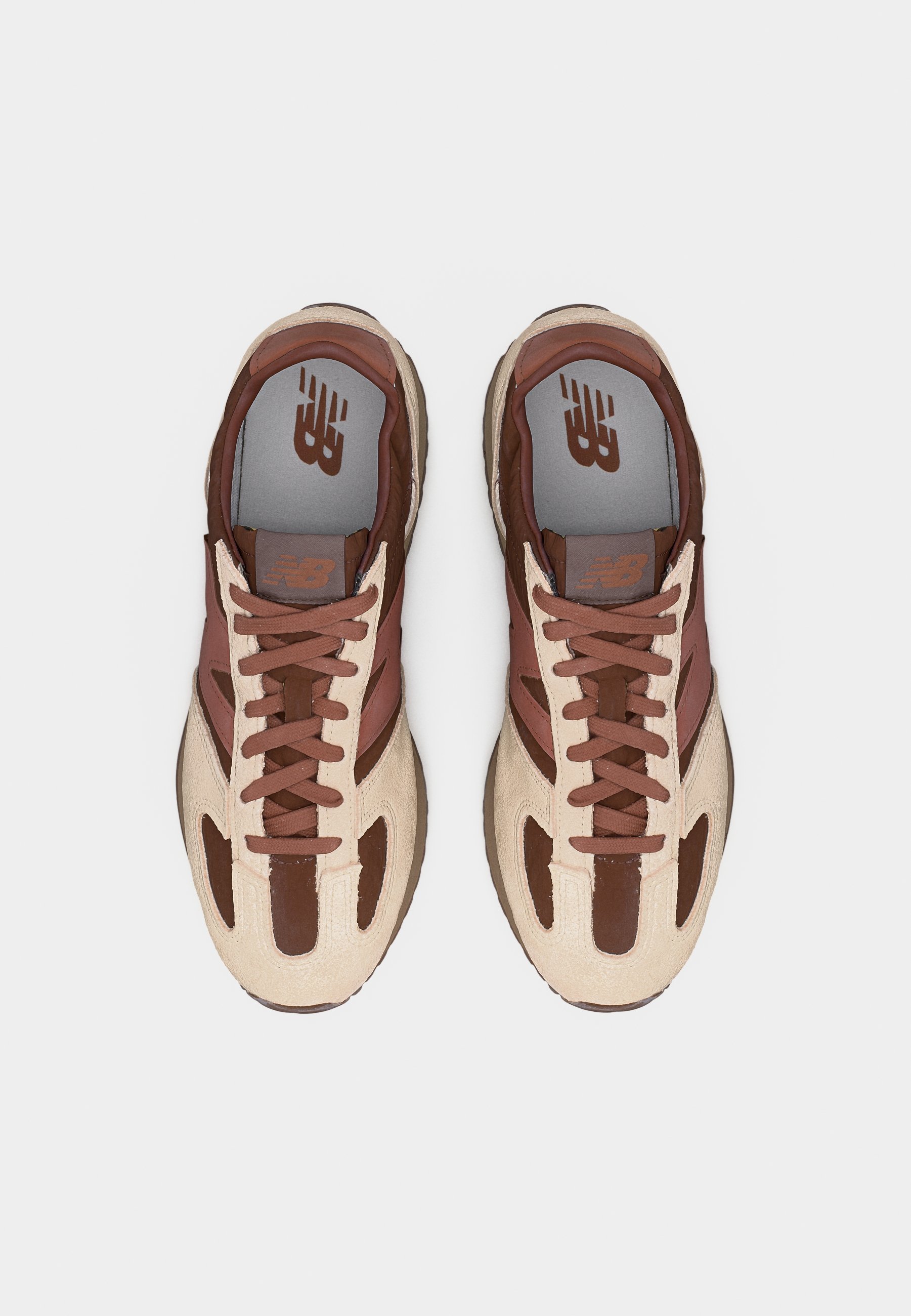 Par de zapatillas New Balance marrones y beige con diseño de cordones vistas desde arriba sobre un fondo blanco.