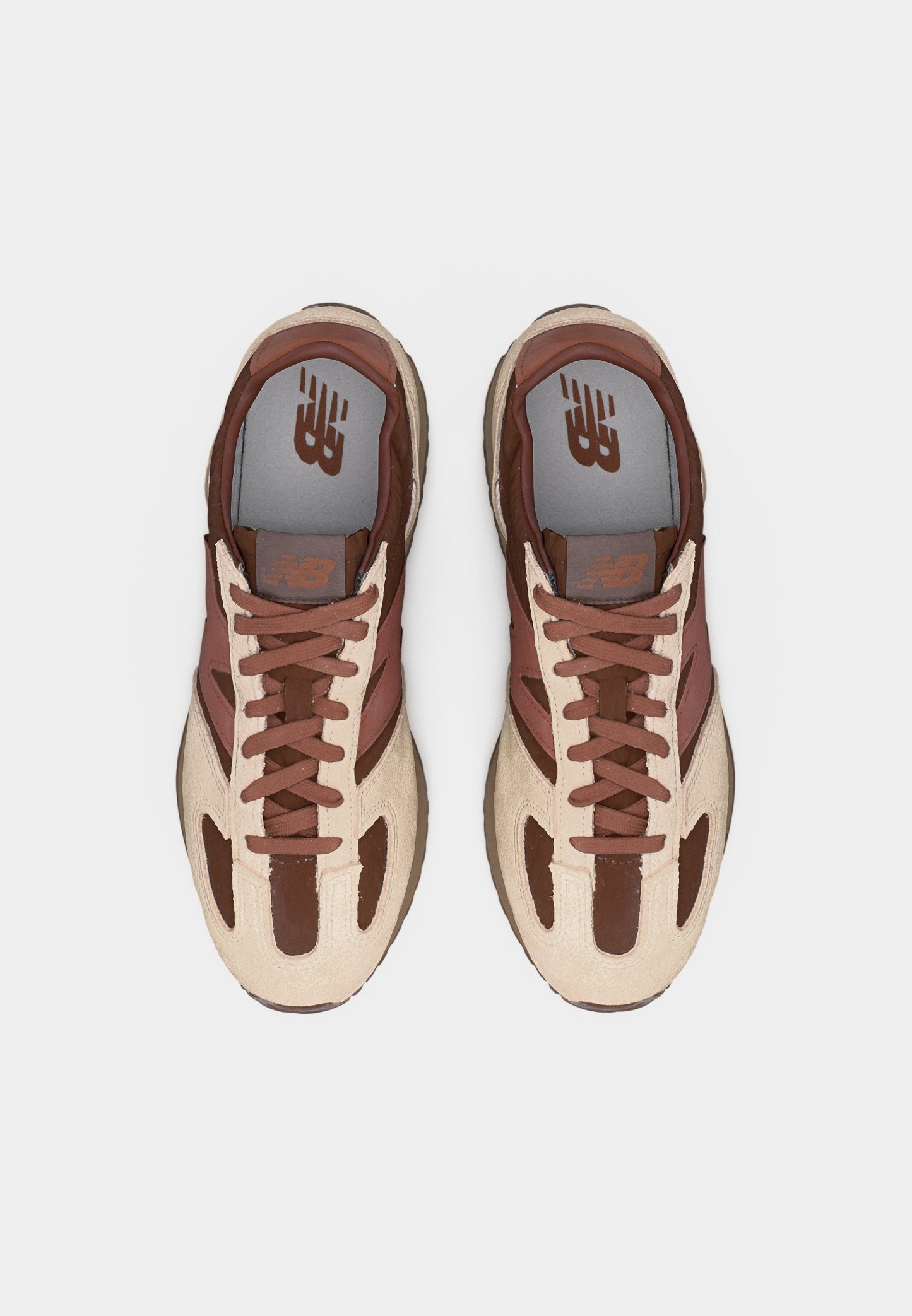 Par de zapatillas New Balance marrones y beige con diseño de cordones vistas desde arriba sobre un fondo blanco.