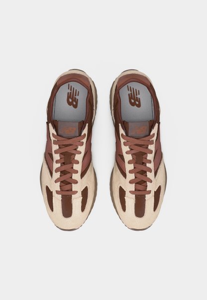 Par de zapatillas New Balance marrones y beige con diseño de cordones vistas desde arriba sobre un fondo blanco.