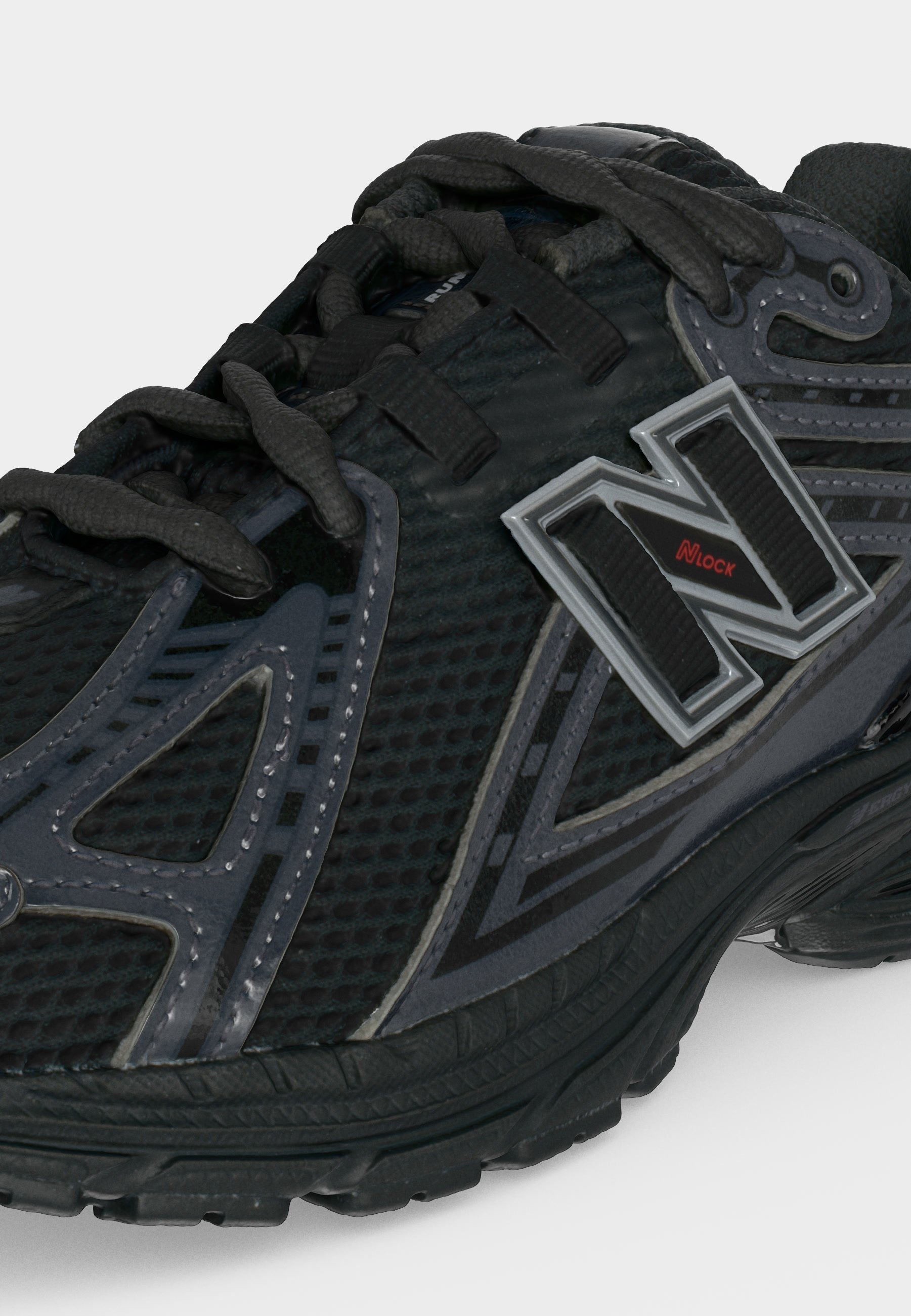 Zapatilla deportiva negra y gris con textura de malla, cierre con cordones y gran logo "N" con texto rojo "NLock" en el lateral.
