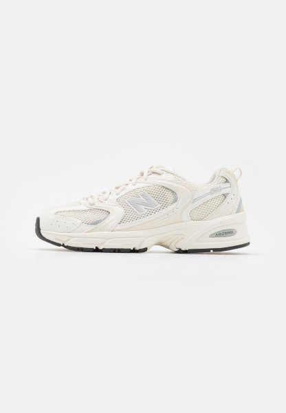 Zapatilla de correr New Balance de malla blanca y gris claro con suela acolchada y banda de rodadura negra, vista de lado.