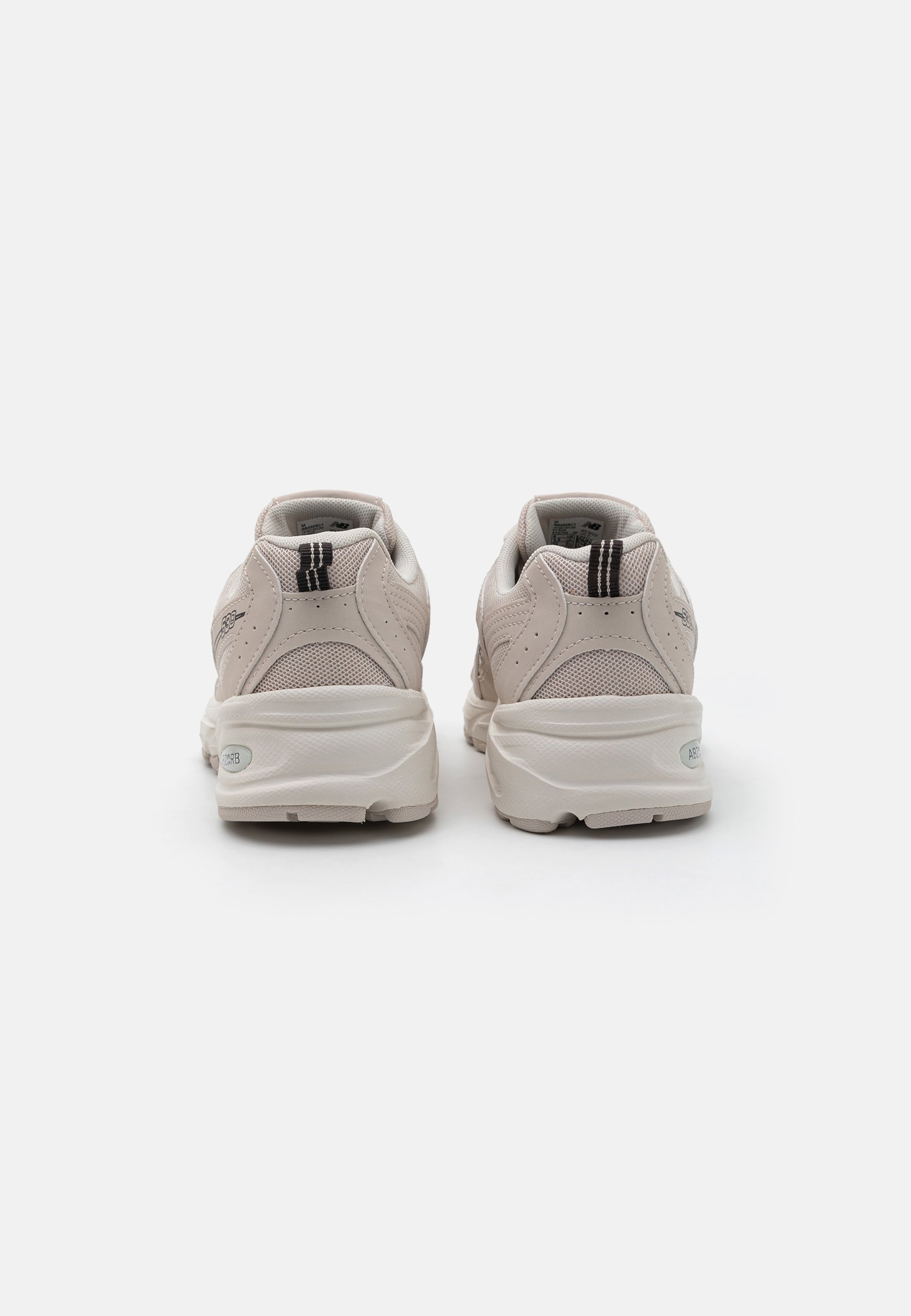 Zapatillas de deporte color beige claro, hechas de material de malla y goma, con forma redondeada, superposiciones texturizadas y un acento de franja negra en el talón.