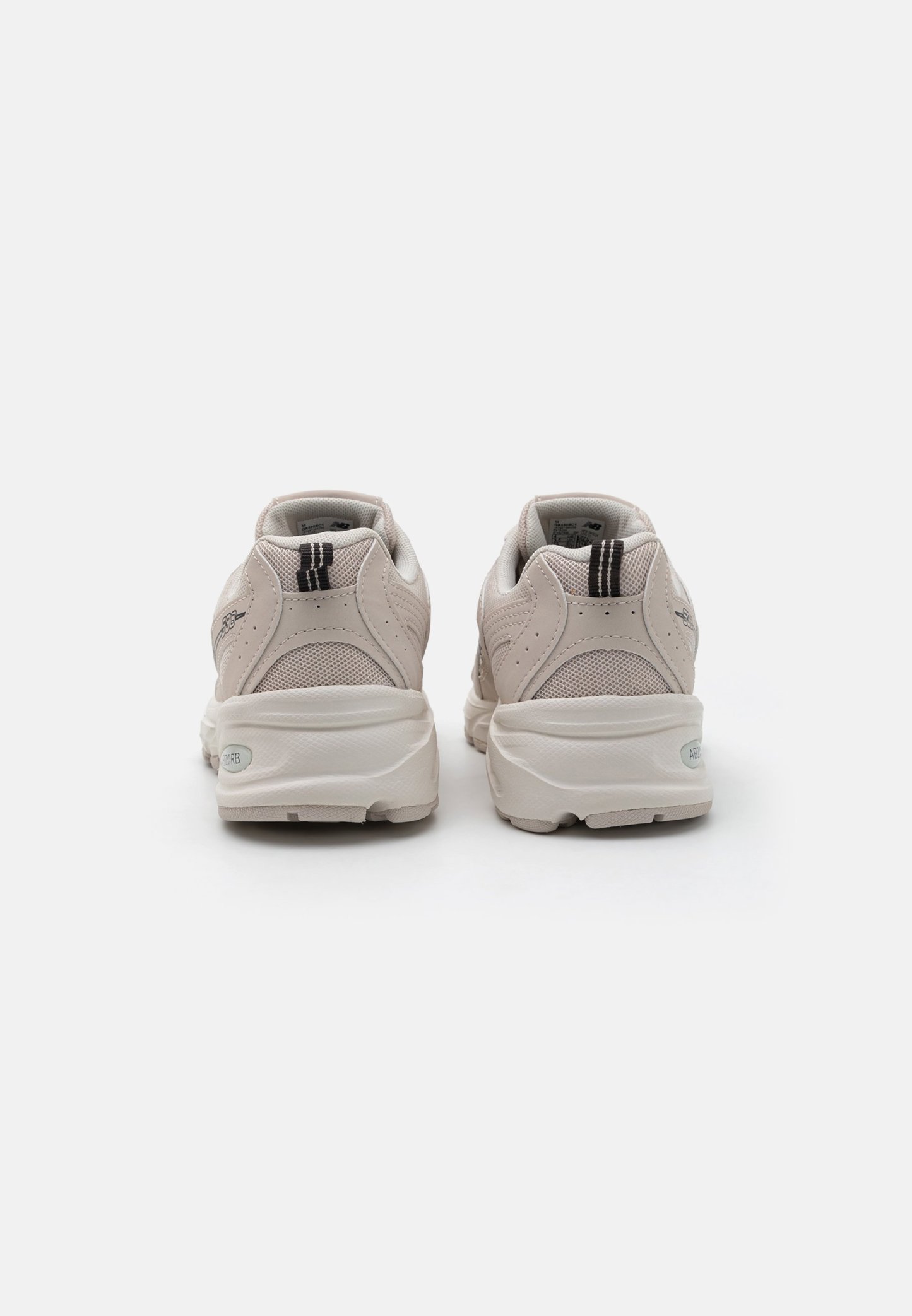 Zapatillas de deporte color beige claro, hechas de material de malla y goma, con forma redondeada, superposiciones texturizadas y un acento de franja negra en el talón.
