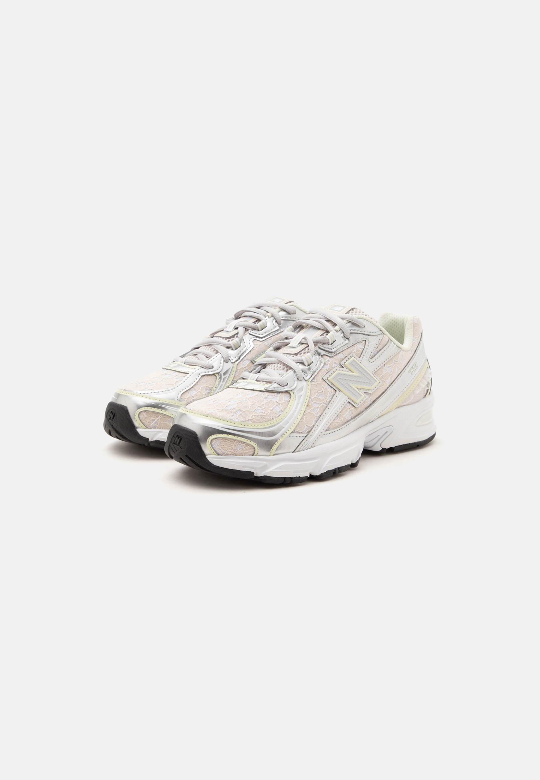 Par de zapatillas de correr New Balance blancas y plateadas con detalles texturizados y suelas negras sobre un fondo claro y liso.