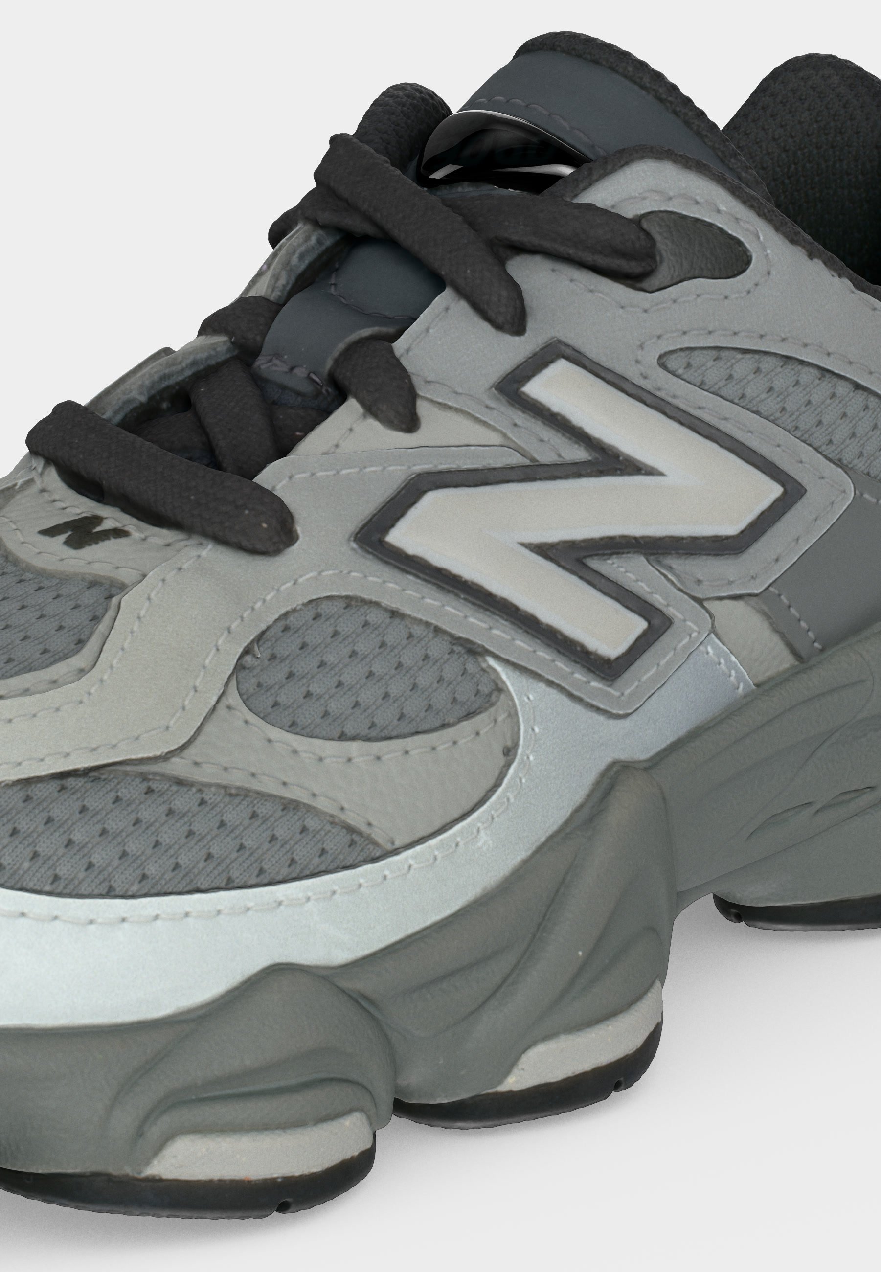 Zapatilla deportiva gris y negra con detalles de malla, suela gruesa, cordones negros y gran logo "N" en el lateral.