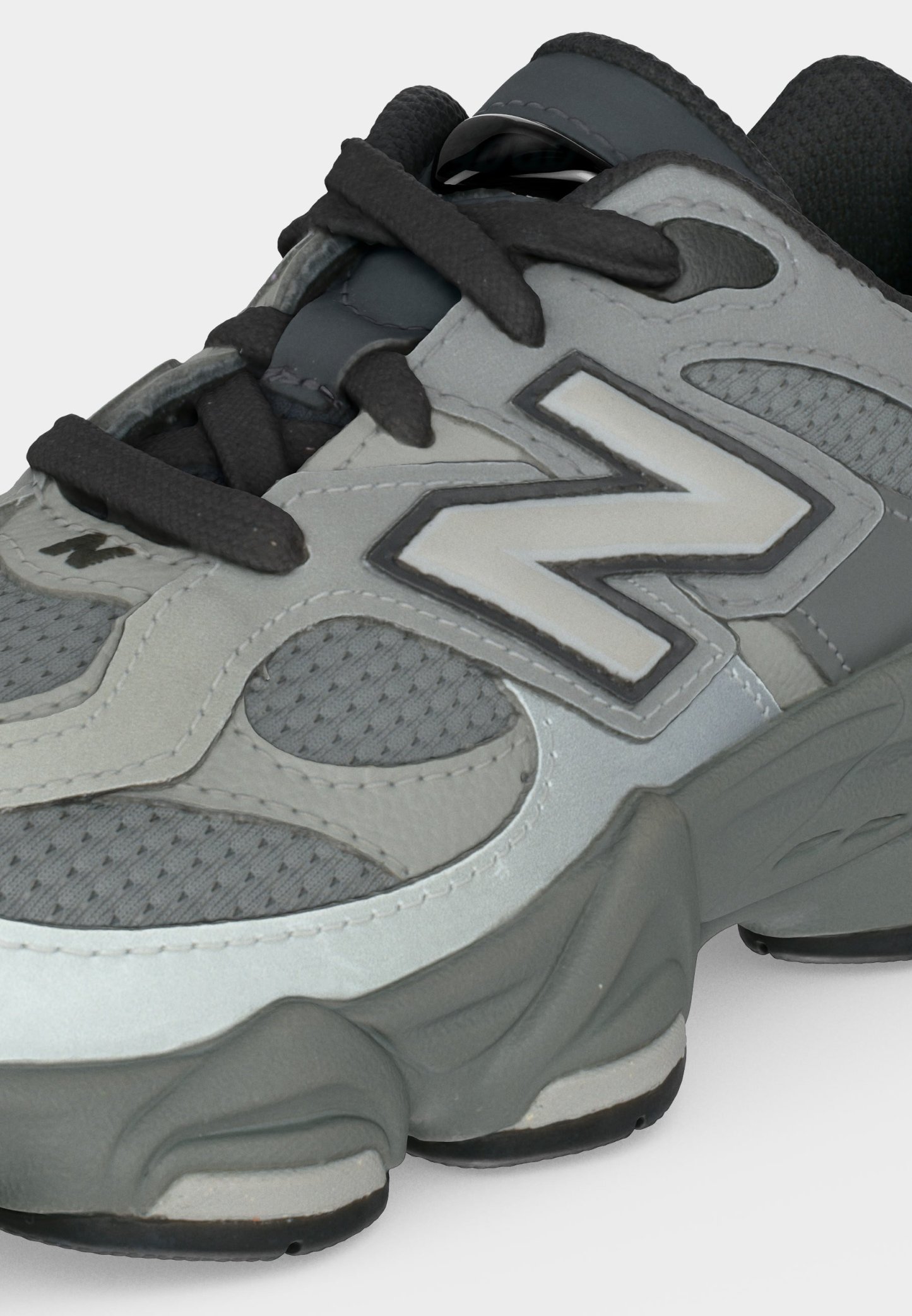 Zapatilla deportiva gris y negra con detalles de malla, suela gruesa, cordones negros y gran logo "N" en el lateral.