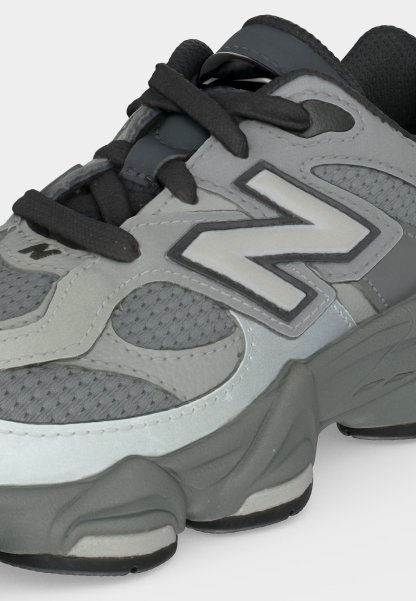 Zapatilla deportiva gris y negra con detalles de malla, suela gruesa, cordones negros y gran logo "N" en el lateral.