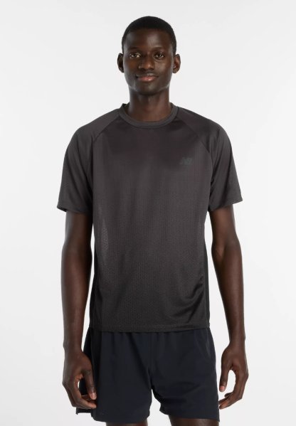 Hombre de pie con una camiseta deportiva negra de manga corta y pantalones cortos negros sobre un fondo blanco liso.