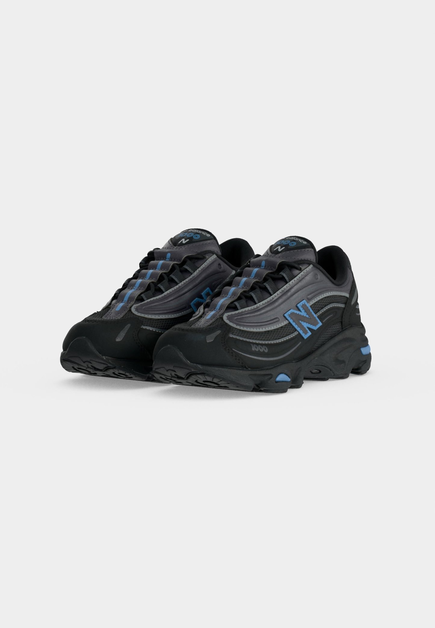 Par de zapatillas deportivas negras y grises con acentos azules y logotipos "N" en los lados, mostradas sobre un fondo blanco.