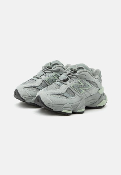 Par de zapatillas deportivas gris claro con paneles de malla y ante, suelas acolchadas y cierre de cordones en un fondo blanco liso.