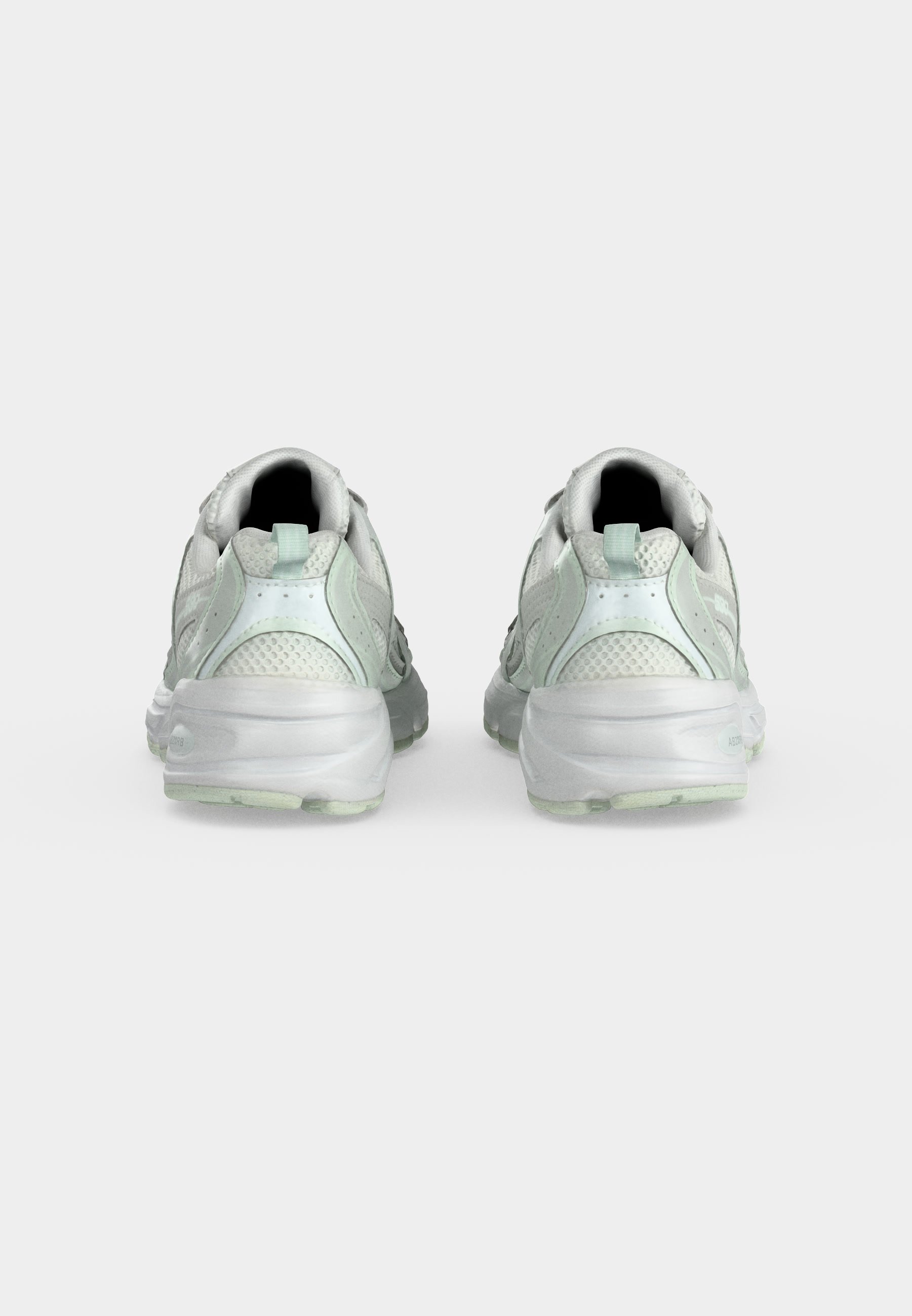 Par de zapatillas deportivas blancas con partes superiores de malla y sintéticas vistas desde atrás sobre un fondo liso y claro.