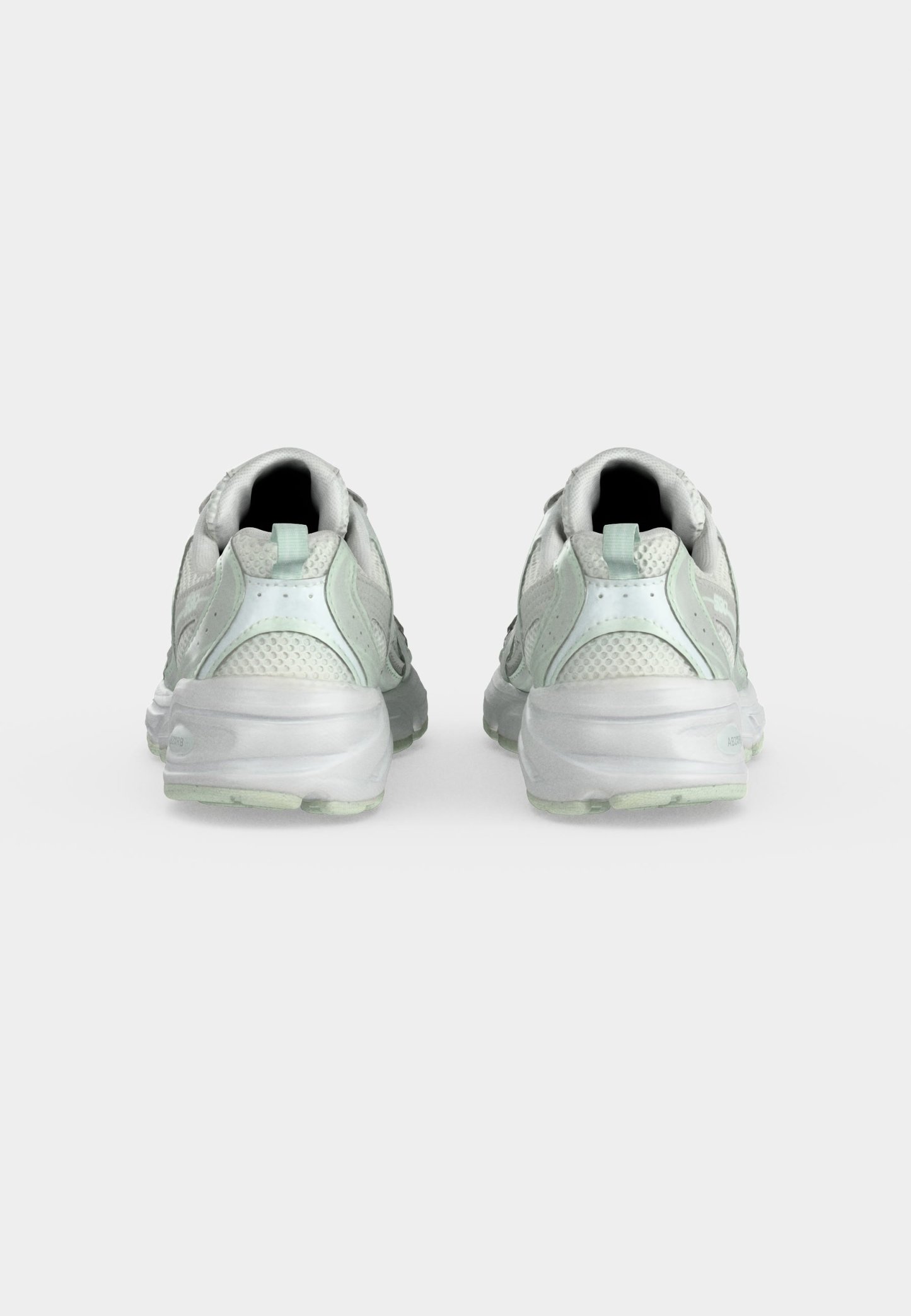 Par de zapatillas deportivas blancas con partes superiores de malla y sintéticas vistas desde atrás sobre un fondo liso y claro.