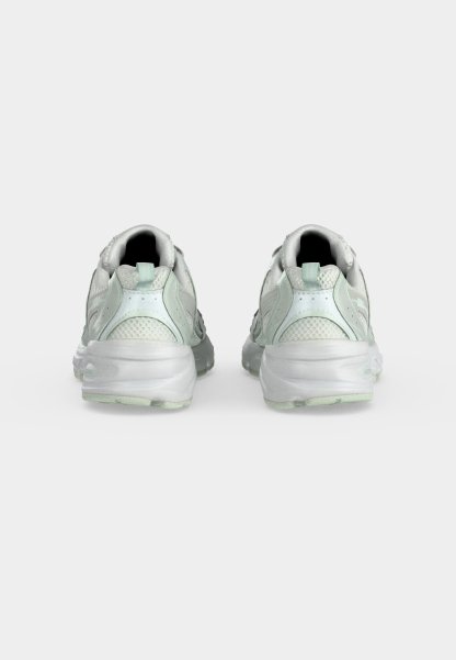 Par de zapatillas deportivas blancas con partes superiores de malla y sintéticas vistas desde atrás sobre un fondo liso y claro.