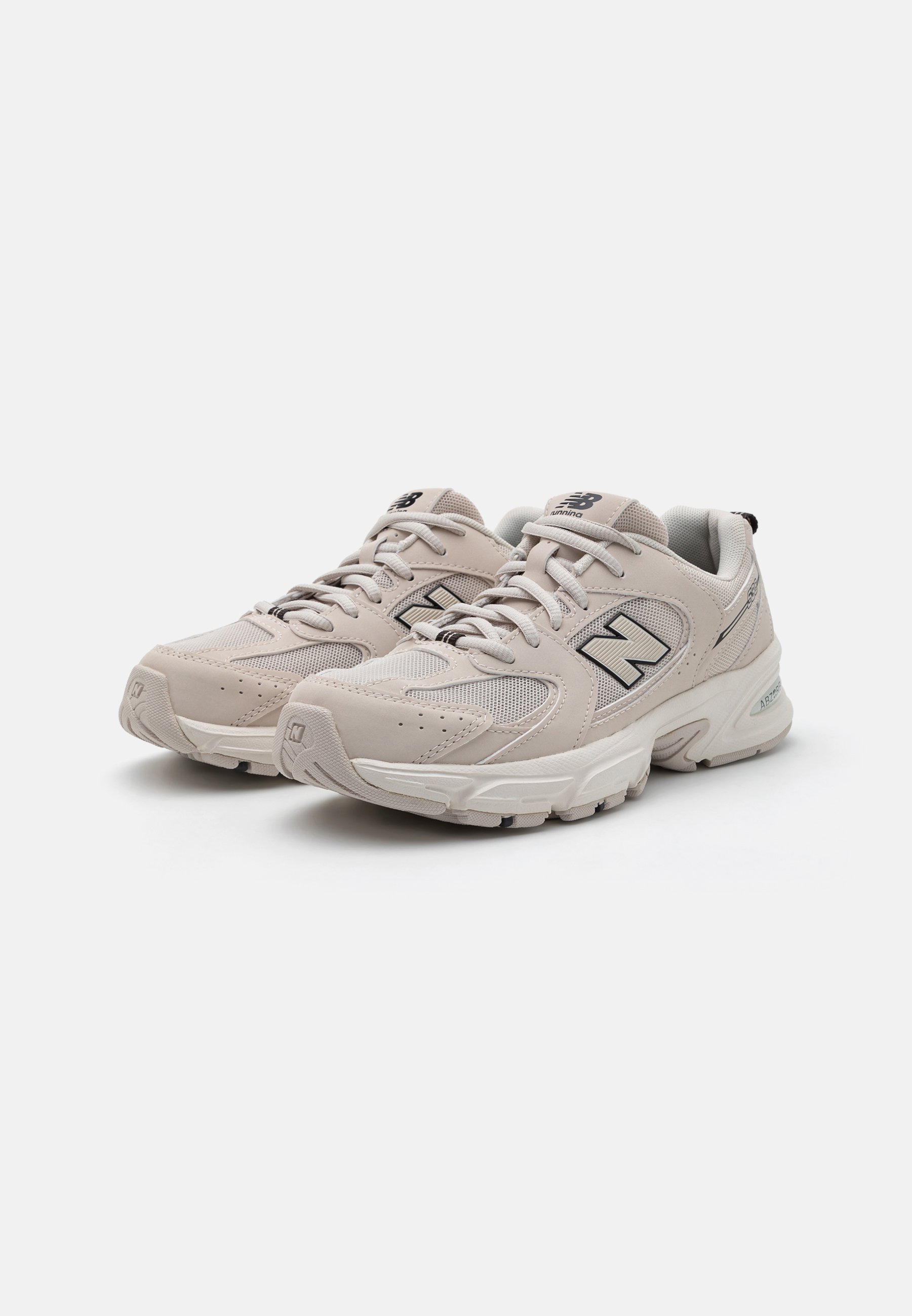 Zapatillas de correr color beige claro con superposición de malla y cuero, punta redondeada, parte frontal con cordones y suela acolchada. Presenta el logo 'N' y acentos texturizados.