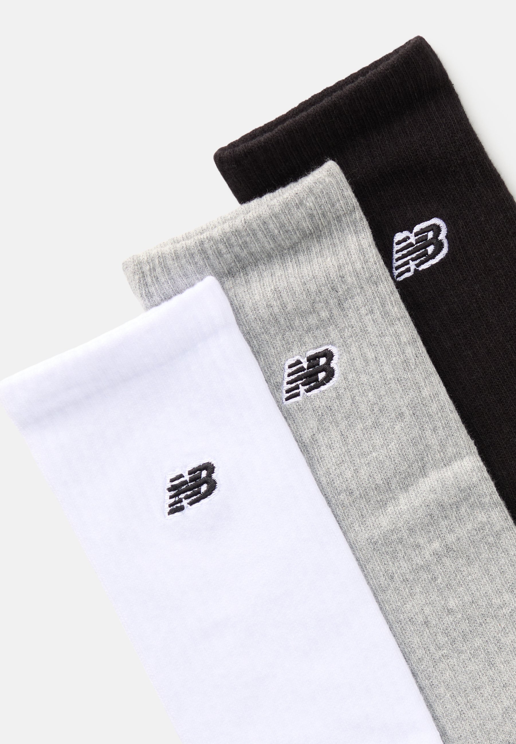 Tres pares de calcetines de vestir en blanco, gris y negro, con un pequeño logo negro de New Balance en cada calcetín. Material de mezcla de algodón, textura acanalada.