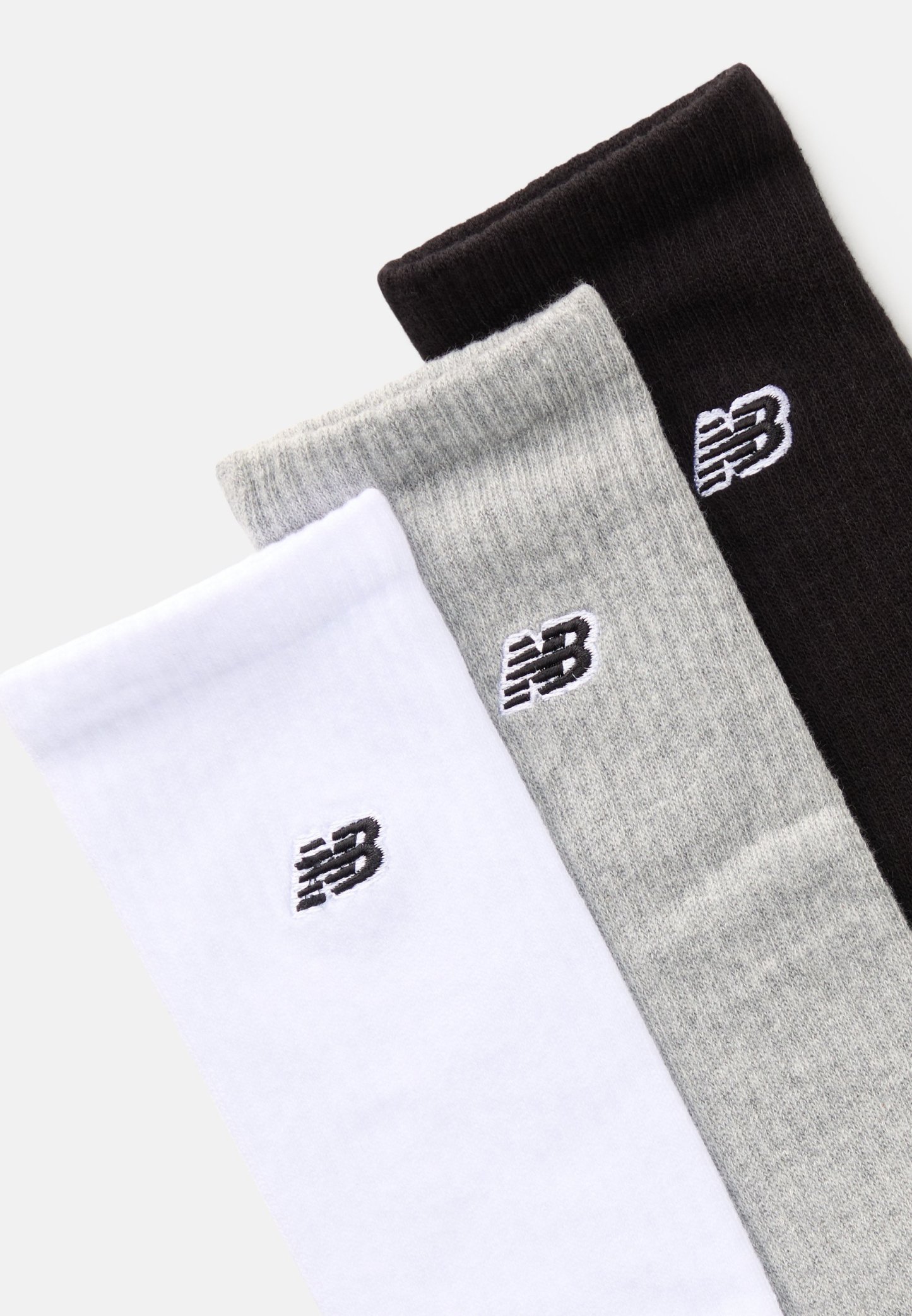 Tres pares de calcetines de vestir en blanco, gris y negro, con un pequeño logo negro de New Balance en cada calcetín. Material de mezcla de algodón, textura acanalada.