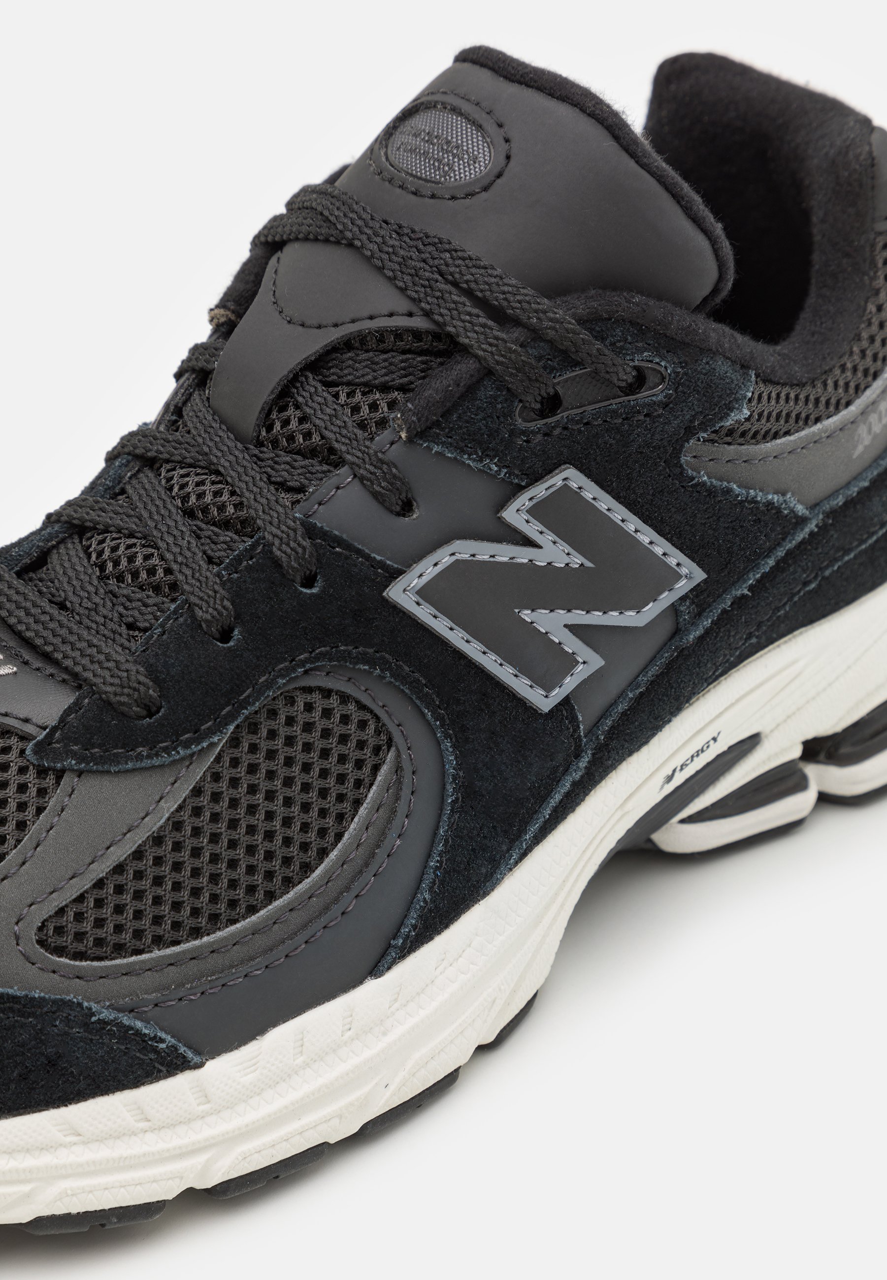 Zapatilla deportiva negra con paneles de malla y ante, con un destacado logotipo plateado "N", cordones texturizados y una suela de caucho blanca.
