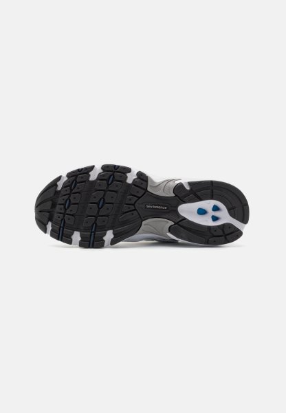 Suela de zapatilla deportiva en negro y gris con superficie de goma texturizada, que presenta un logo, patrón de suela y detalles en azul.
