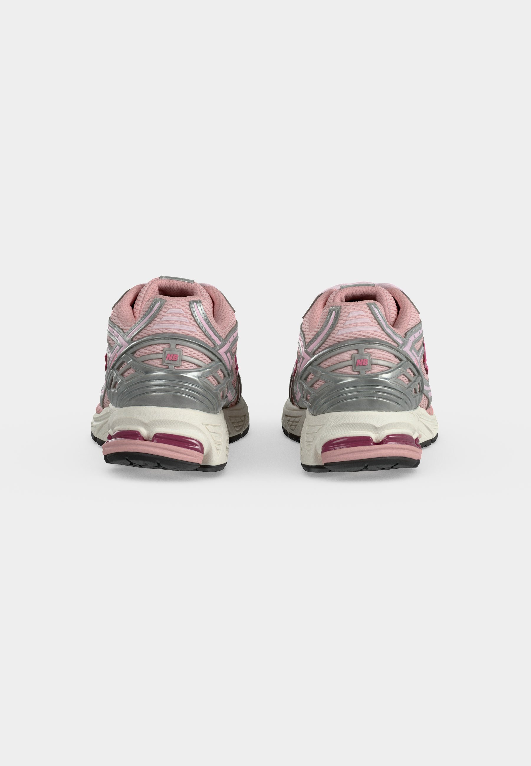 Par de zapatillas deportivas rosas y plateadas vistas desde atrás sobre un fondo liso gris claro.