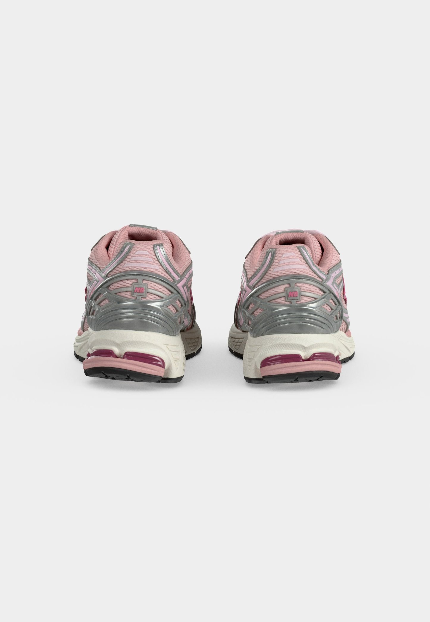Par de zapatillas deportivas rosas y plateadas vistas desde atrás sobre un fondo liso gris claro.