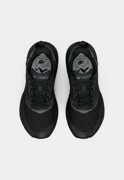 Zapatos deportivos negros con parte superior de malla, suela de goma texturizada, acentos reflectantes y un cuello acolchado. Presenta un diseño con cordones.