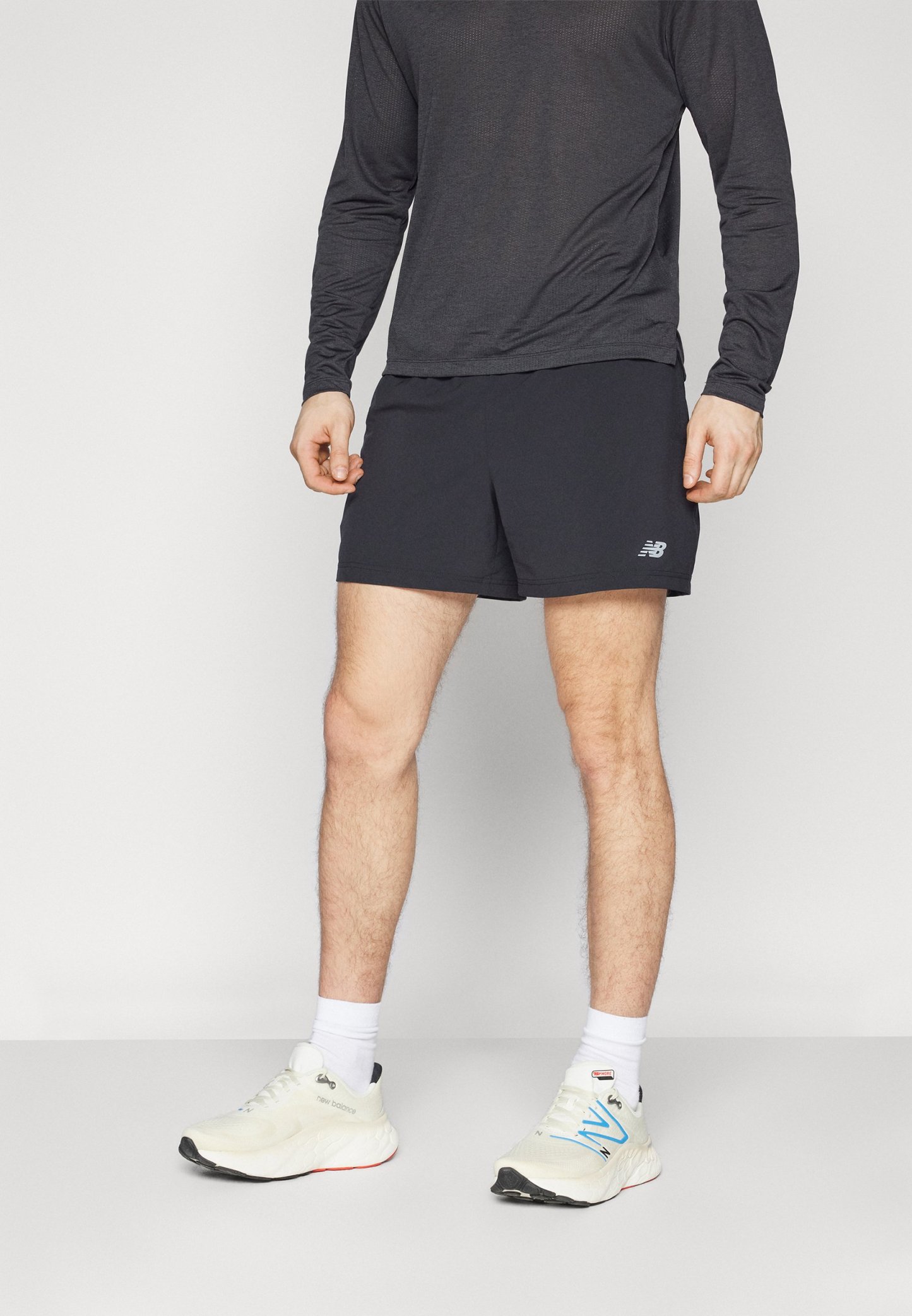 Pantalones cortos deportivos negros con un logo en la pierna izquierda, combinados con una camiseta de manga larga gris oscuro y zapatillas blancas.