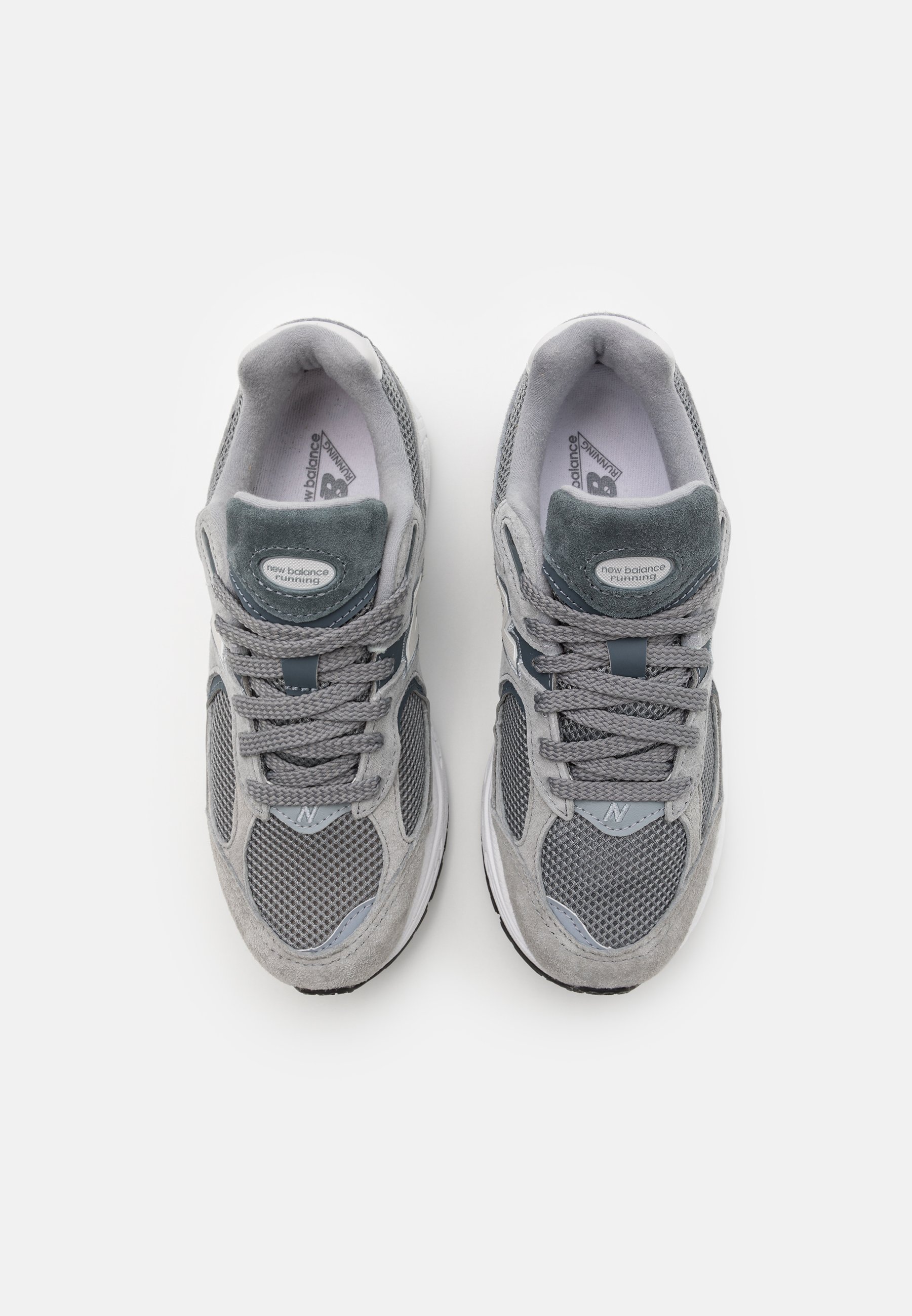 Las zapatillas deportivas grises presentan una parte superior de malla con detalles de ante, un collar acolchado y cordones tonales. Las suelas son blancas con un relieve texturizado.