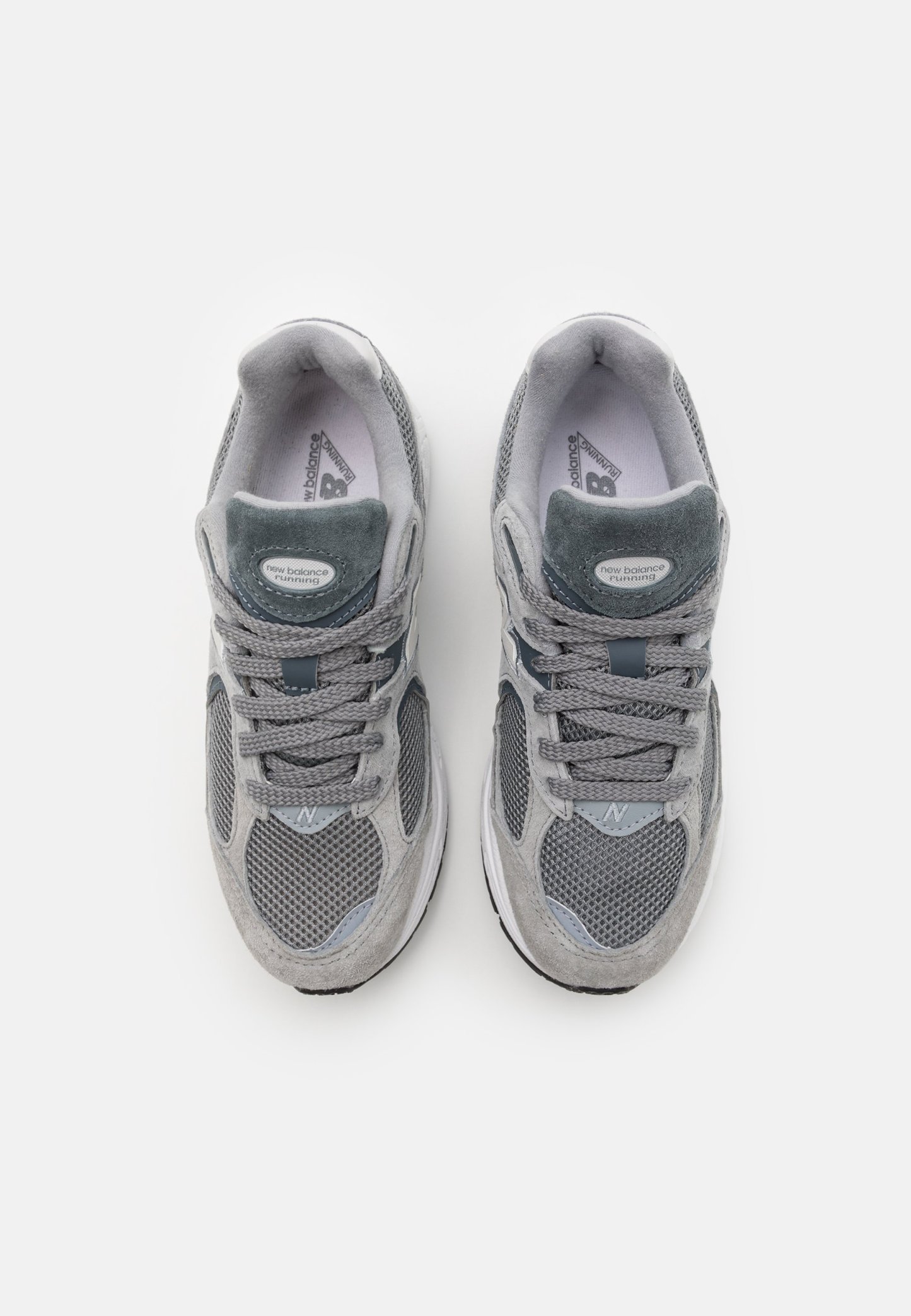 Las zapatillas deportivas grises presentan una parte superior de malla con detalles de ante, un collar acolchado y cordones tonales. Las suelas son blancas con un relieve texturizado.