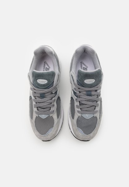 Las zapatillas deportivas grises presentan una parte superior de malla con detalles de ante, un collar acolchado y cordones tonales. Las suelas son blancas con un relieve texturizado.