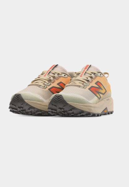 Par de zapatillas para correr por senderos en beige y naranja con suelas gruesas negras con dibujo y logo rojo en los costados, fotografiadas sobre un fondo blanco.