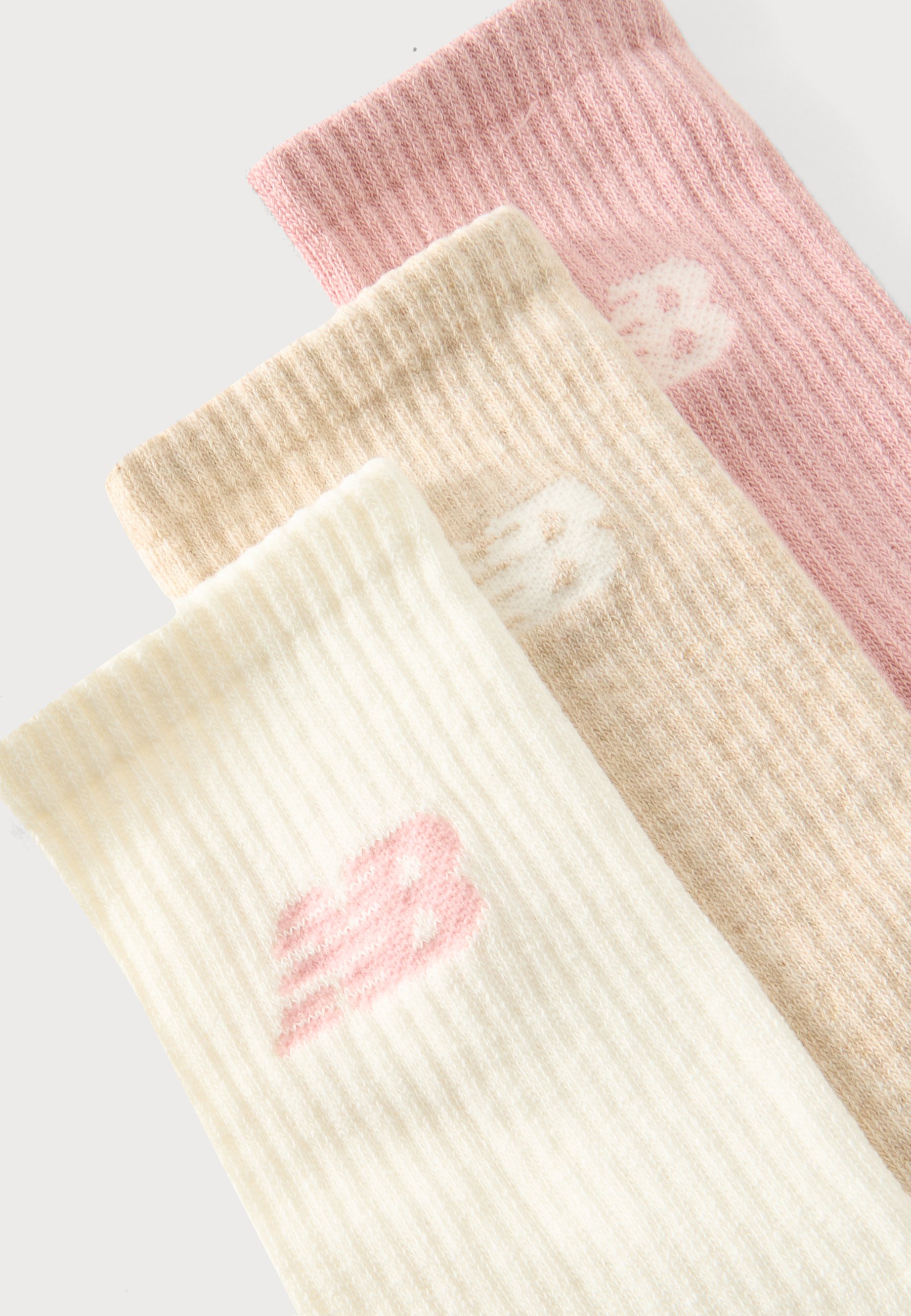 Tres calcetines de punto acanalado en rosa, beige y blanco, cada uno con un pequeño logo estilizado "B" cerca del puño superior.