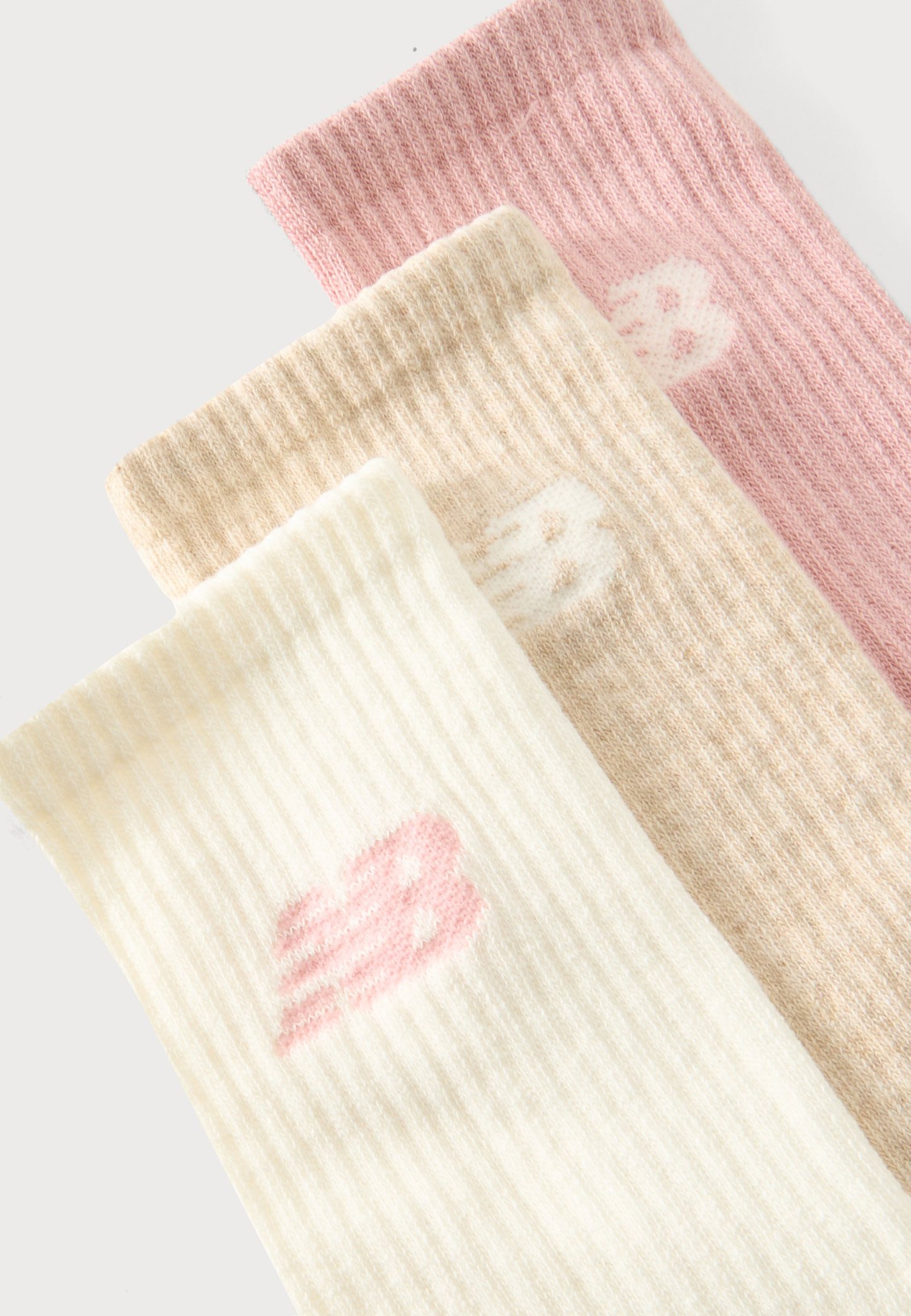 Tres calcetines de punto acanalado en rosa, beige y blanco, cada uno con un pequeño logo estilizado "B" cerca del puño superior.
