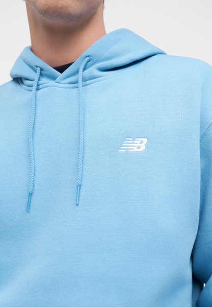 Hombre con sudadera con capucha azul claro con cordones y un pequeño logo blanco de New Balance en el pecho sobre un fondo sencillo.