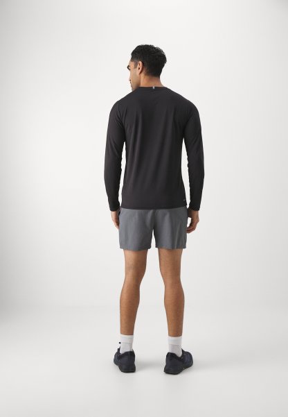 Camiseta de manga larga negra para hombre con cuello redondo, combinada con pantalones cortos grises. La persona se presenta de espaldas, mostrando un diseño ajustado y calzado deportivo.