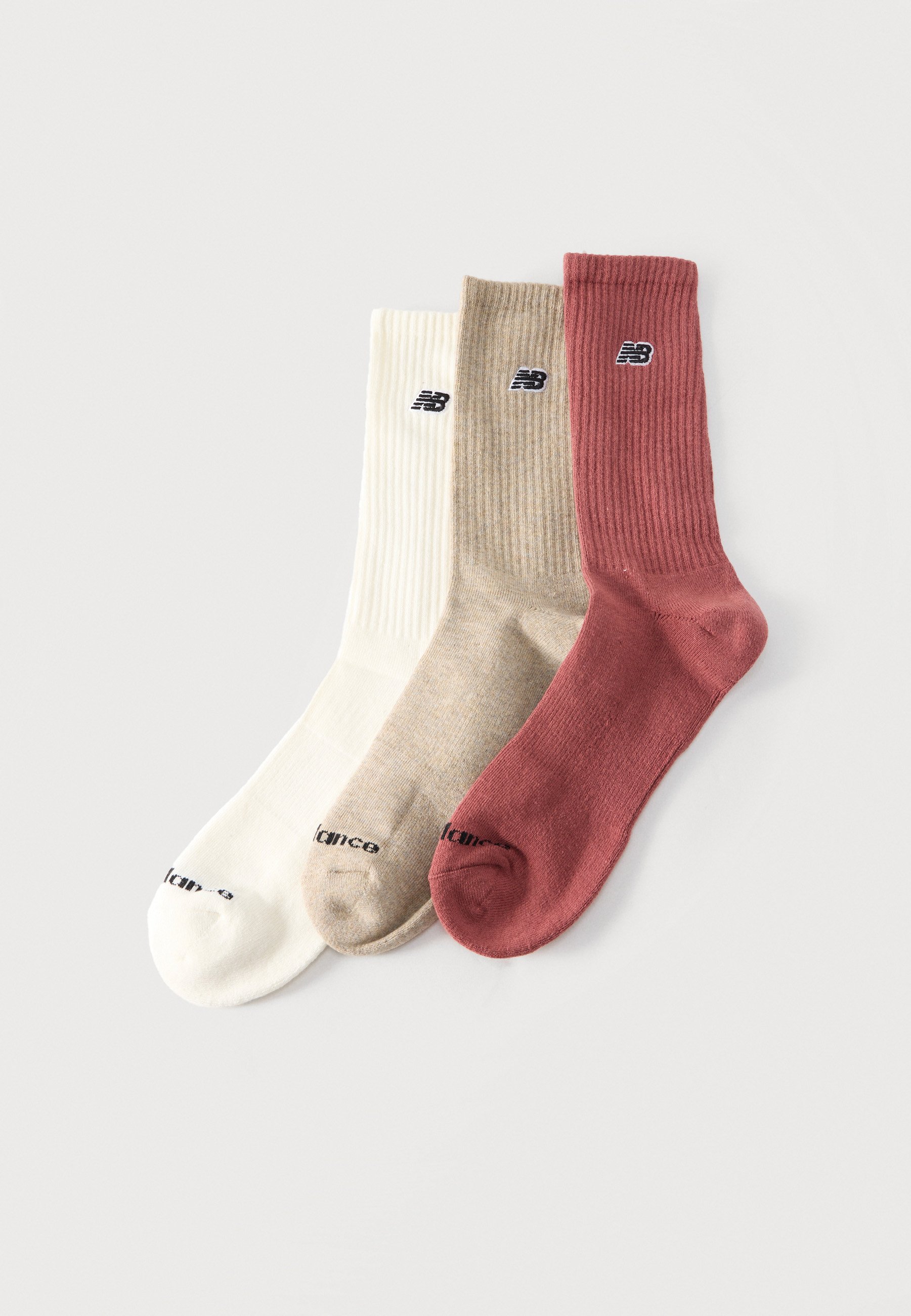 Tres calcetines New Balance de canalé para hombre en blanco, beige y óxido, colocados uno al lado del otro sobre un fondo liso.