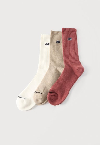 Tres calcetines New Balance de canalé para hombre en blanco, beige y óxido, colocados uno al lado del otro sobre un fondo liso.