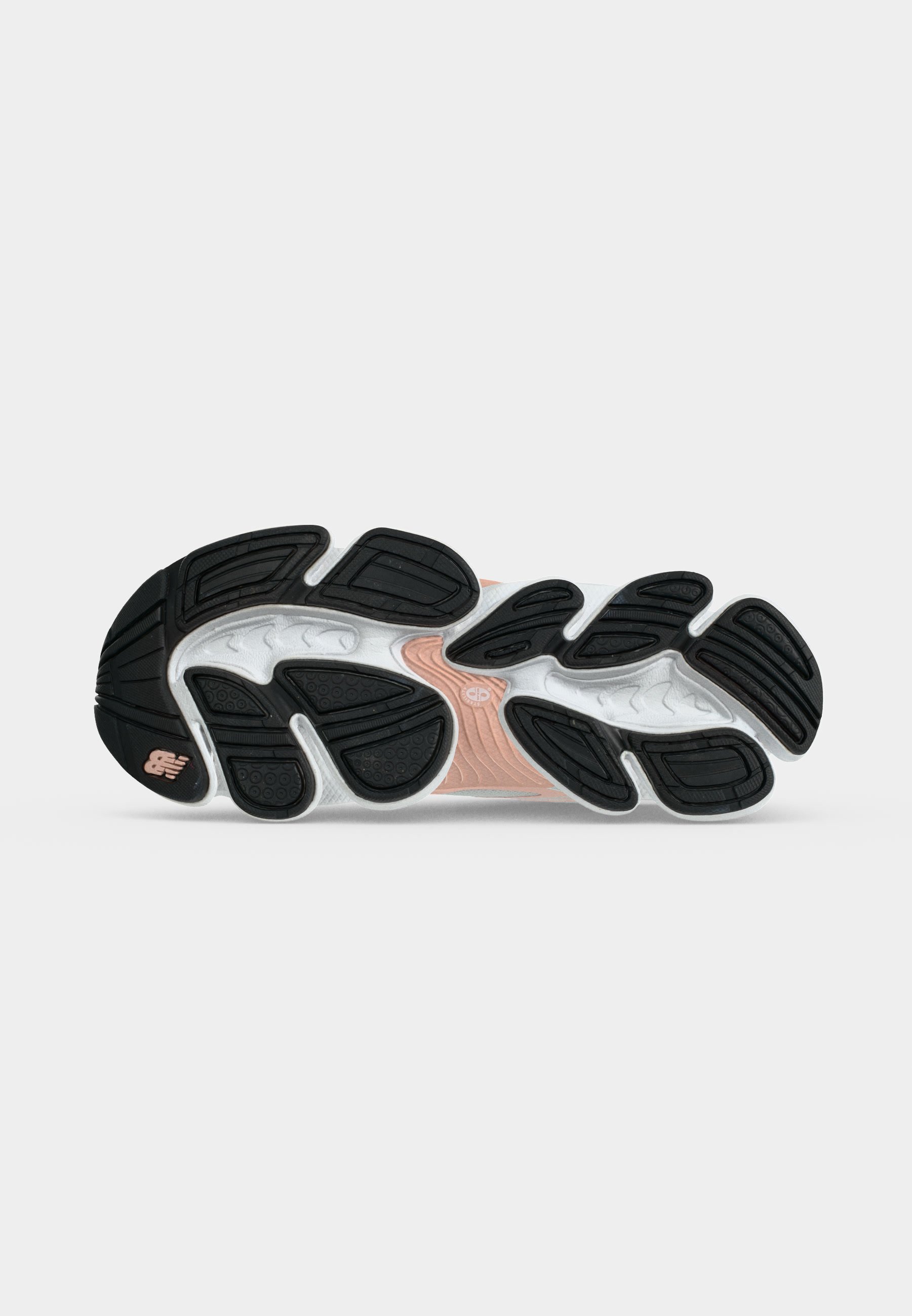 Suela de zapato con almohadillas de tracción de caucho negro y ranuras blancas, con una sección media de color melocotón y un pequeño logotipo de la marca cerca del talón.