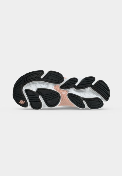 Suela de zapato con almohadillas de tracción de caucho negro y ranuras blancas, con una sección media de color melocotón y un pequeño logotipo de la marca cerca del talón.