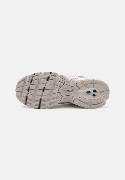 Suela de zapatilla en blanco roto con agarre de goma texturizada, presentando acentos en negro y azul, diseño ergonómico y patrones de relieve distintivos para tracción.