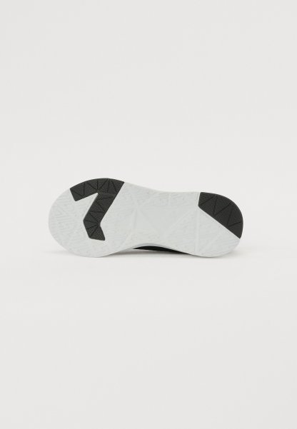 Suela de zapatilla deportiva en goma negra con una capa texturizada blanca; presenta patrones de tracción geométricos para agarre y estabilidad.