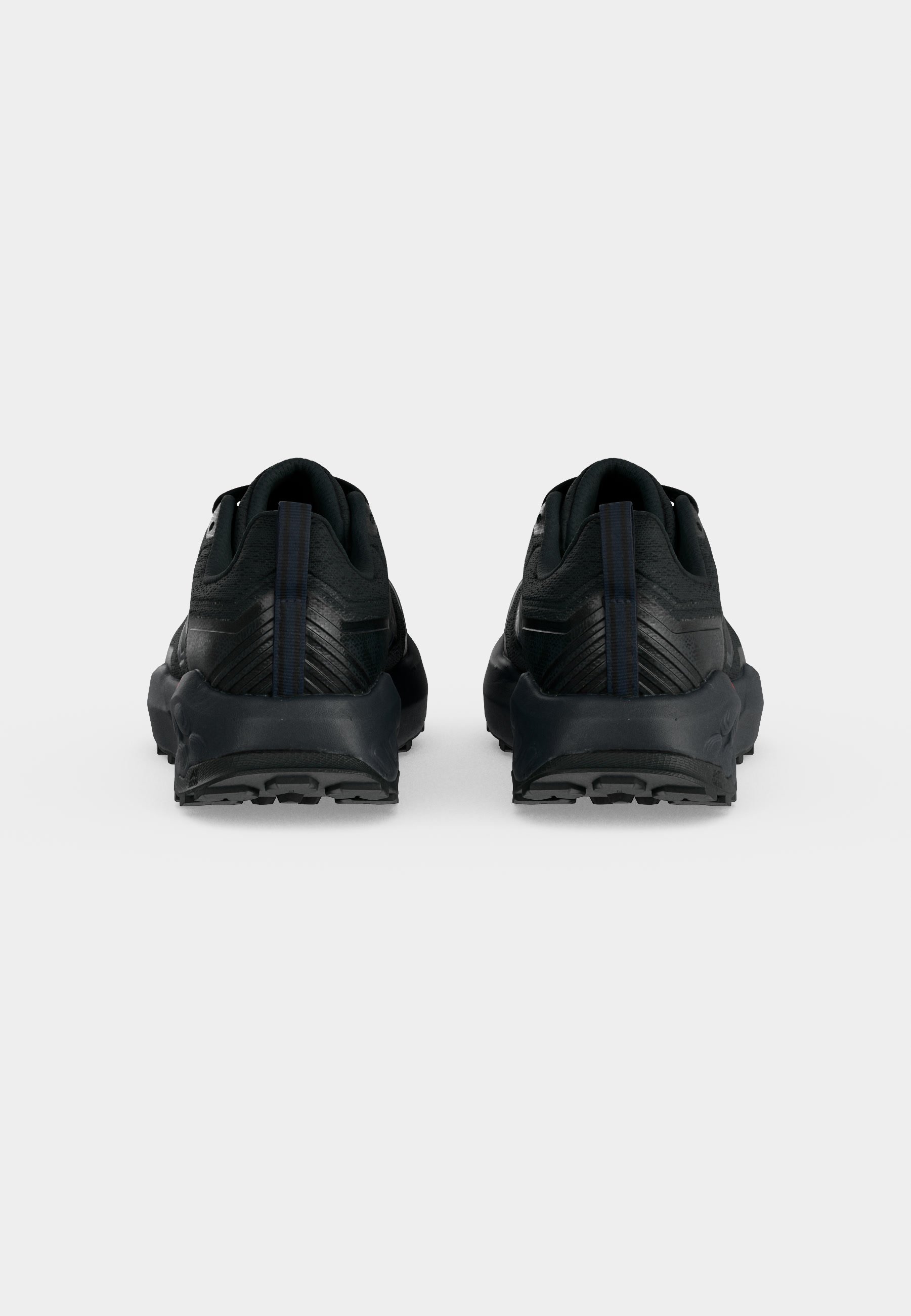 Par de zapatillas deportivas negras vistas desde atrás con suelas texturizadas y lengüetas verticales en un fondo claro y liso.