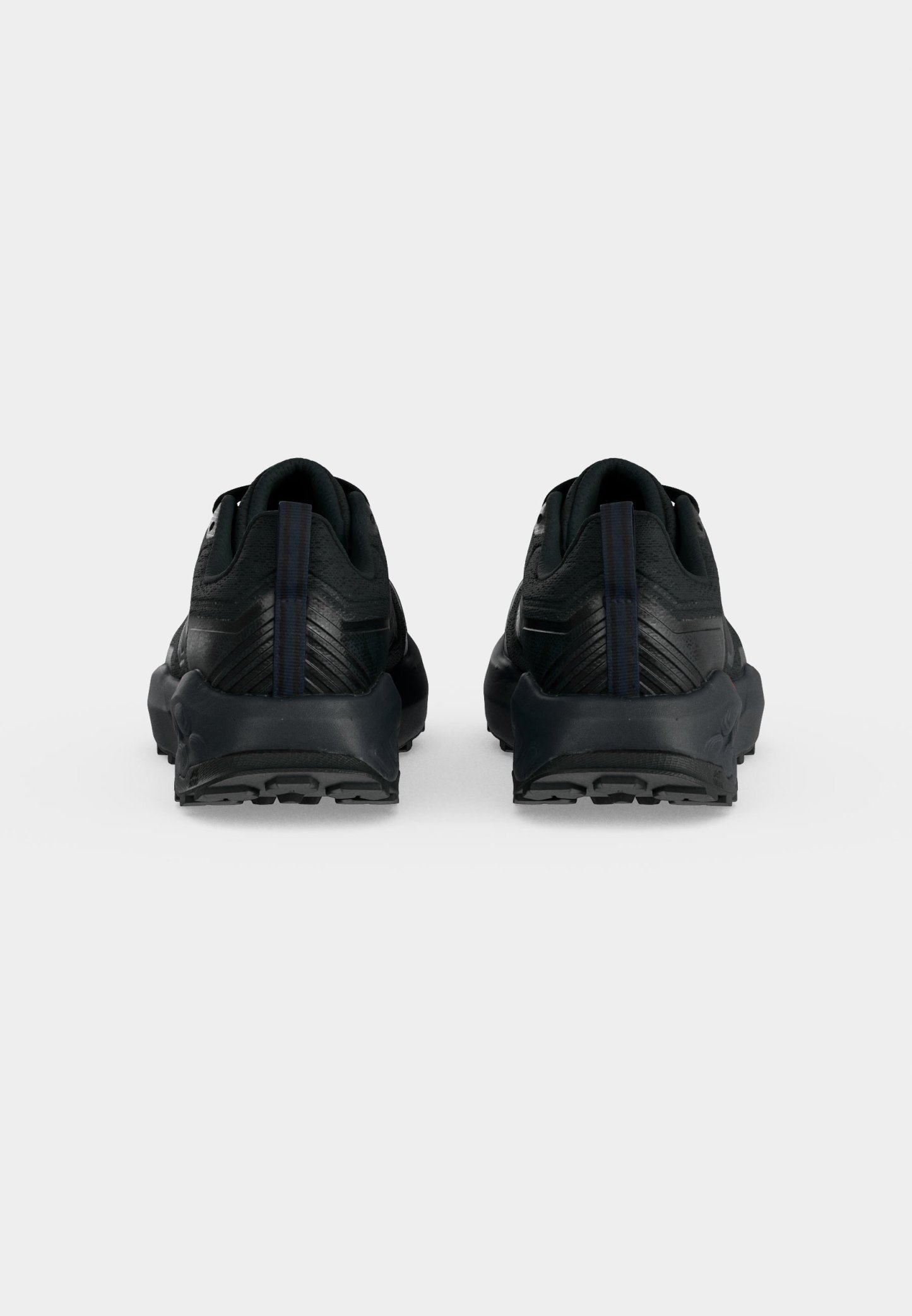 Par de zapatillas deportivas negras vistas desde atrás con suelas texturizadas y lengüetas verticales en un fondo claro y liso.