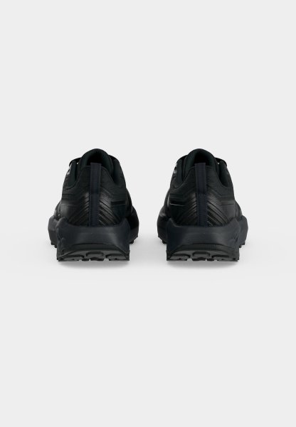 Par de zapatillas deportivas negras vistas desde atrás con suelas texturizadas y lengüetas verticales en un fondo claro y liso.