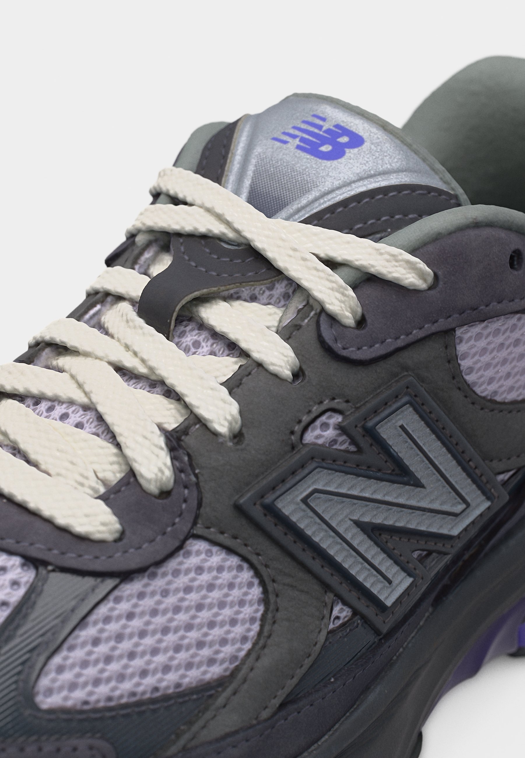 Primer plano de una zapatilla New Balance gris y morada con cordones blancos y tejido de malla en la parte superior del zapato.