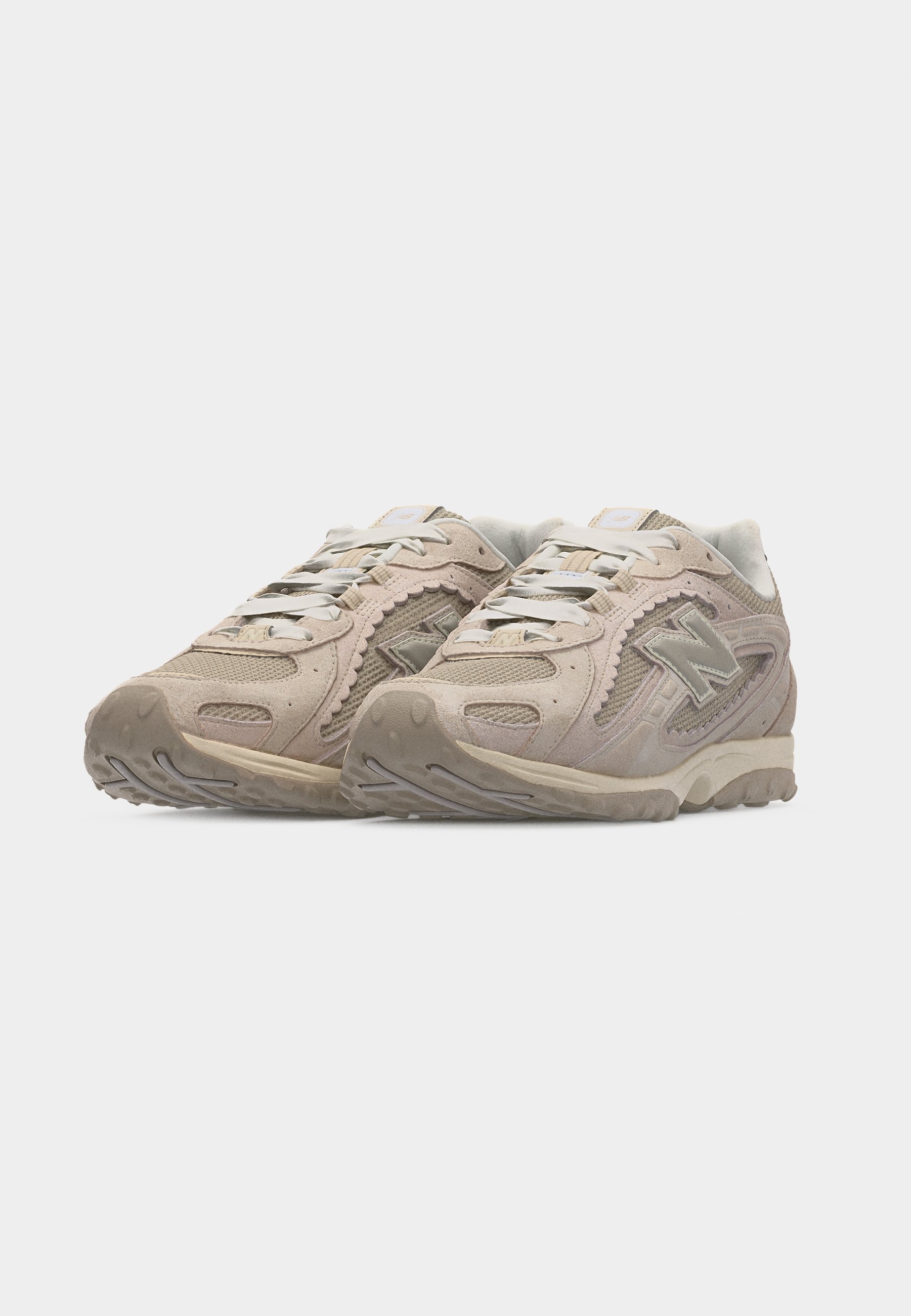 Par de zapatillas New Balance beige con detalles de malla y ante, cordones blancos y suelas de goma texturizadas sobre un fondo blanco.