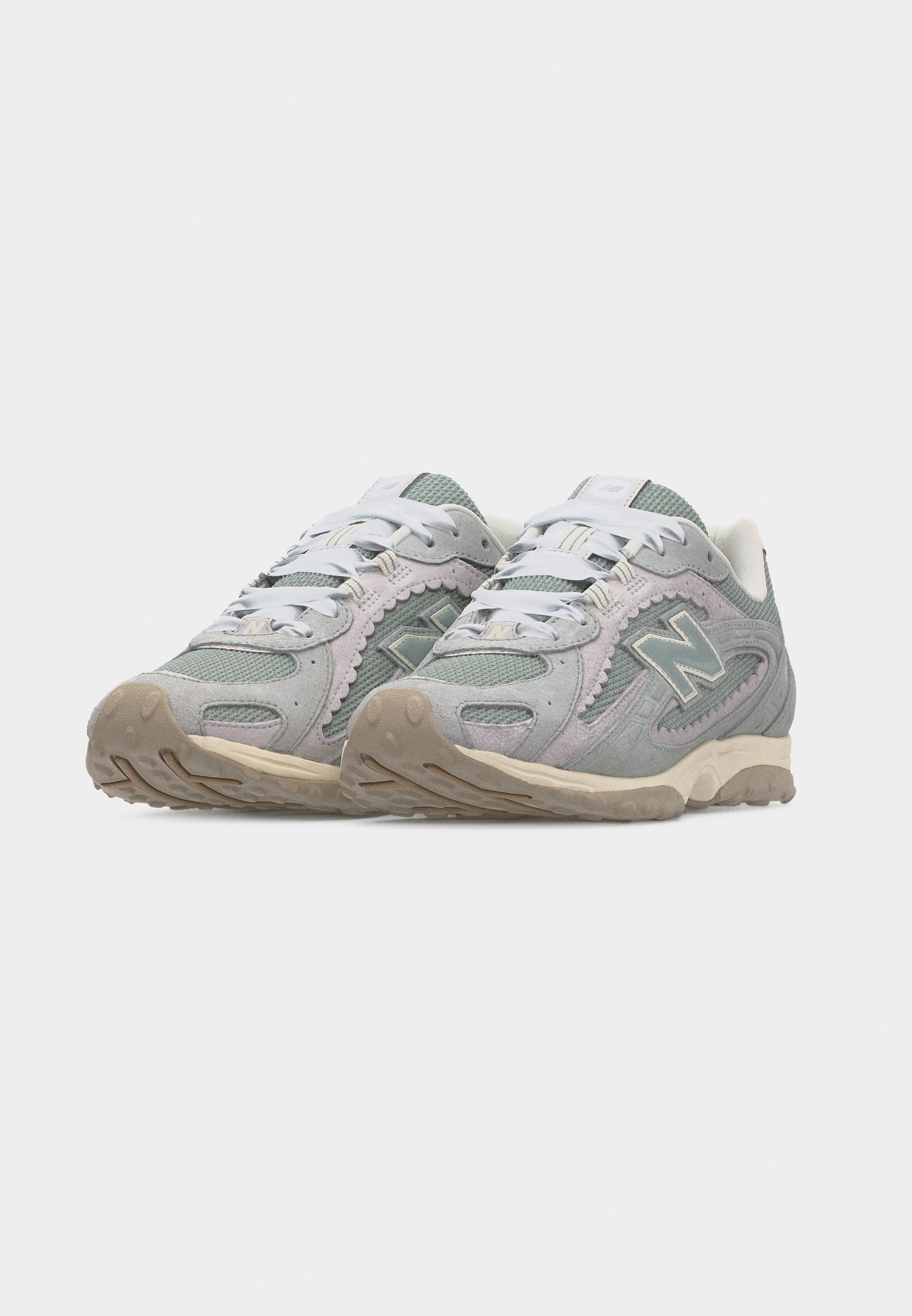 Par de zapatillas New Balance en gris y beige con cordones blancos y suelas texturizadas, mostradas desde un ángulo frontal izquierdo sobre fondo blanco.