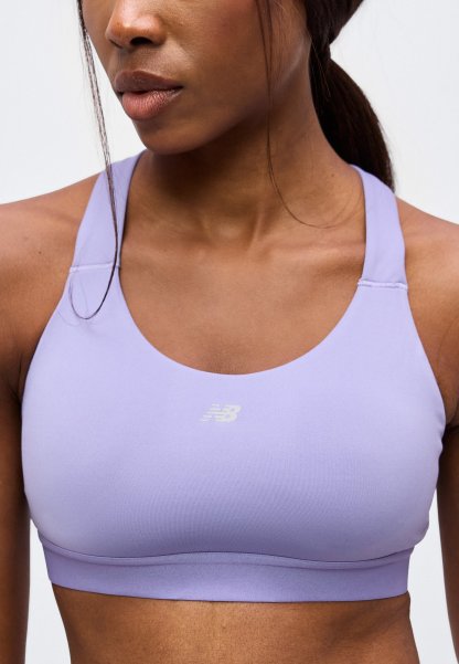 Mujer con sujetador deportivo New Balance de color lila claro, cabello recogido, recortada a la altura de los hombros y el abdomen con fondo blanco.
