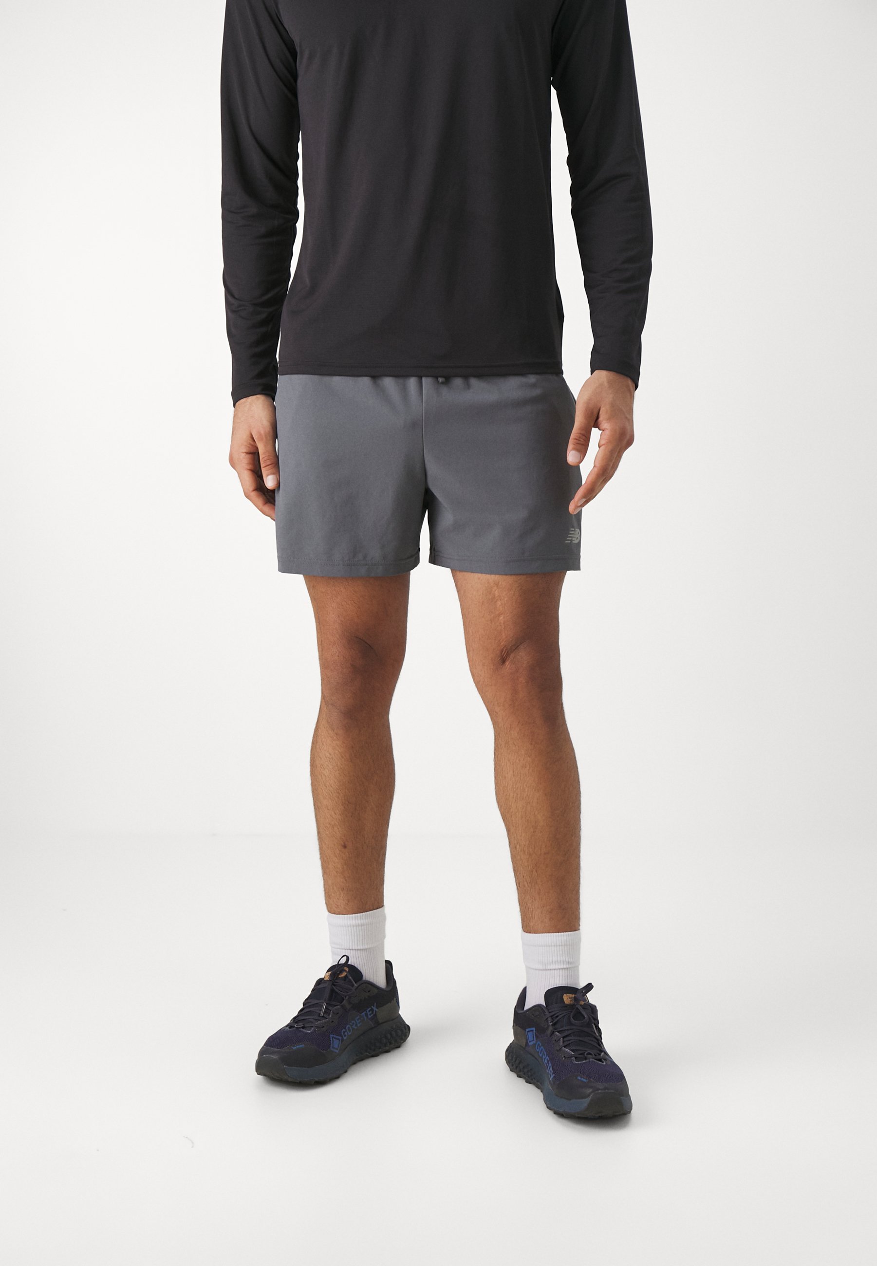 Pantalones cortos deportivos de tela gris con una cinturilla elástica. Llevados con una camiseta negra de manga larga y zapatos oscuros con detalles azules.