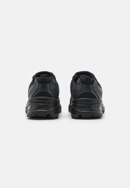 Zapatillas deportivas negras con parte superior de malla y suela de goma, que cuentan con acentos texturizados, tacón redondeado y una lengüeta en la parte trasera para facilitar el calzado.